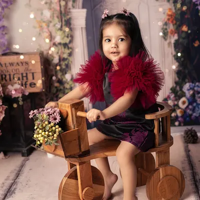 Pedaling through a garden of dreams on her little wooden trike. This whimsical setup, with its floral backdrop and soft lighting, creates a magical, fairytale-like portrait.