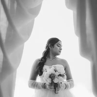 A stunning black and white bridal portrait, framed by curtains. The high-contrast lighting creates a dramatic and timeless feel, focusing on the bride's silhouette.