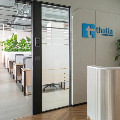 The entrance to the Thalia Technologies office, featuring a clean, modern reception desk with fluted details. The frosted glass door offers a hint of the bright, open workspace within, creating a welcoming first impression.