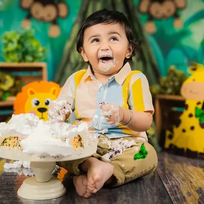 The best part of a cake smash! This little boy is having the time of his life, covered in cake and smiling from ear to ear in a jungle-themed setup.