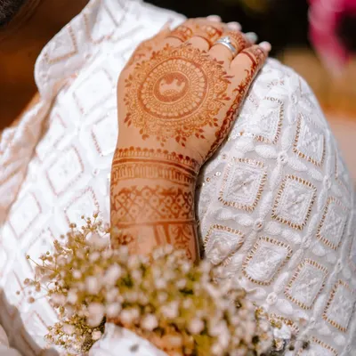 A simple, beautiful detail. This close-up shot focuses on the bride's intricate mehendi as her hand rests on her partner's shoulder, a symbol of their new bond.