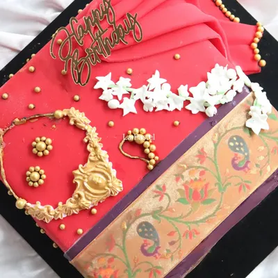 A top-down view of my signature Paithani saree cake. You can see the handcrafted edible necklace, nose ring, and jasmine flower gajra, all resting on the vibrant red fondant saree.