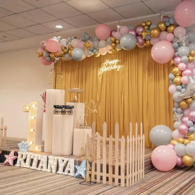 A wider view of the elegant first birthday setup for Ritanya. The combination of a golden curtain backdrop, a neon sign, and a full balloon arch creates a rich and celebratory feel for the main photo area.