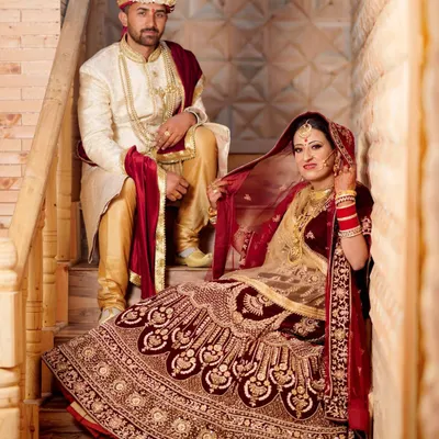 An elegant, royal-style wedding portrait of the couple posed on a wooden staircase. The bride's rich, velvet lehenga and the groom's sherwani create a timeless and regal look.