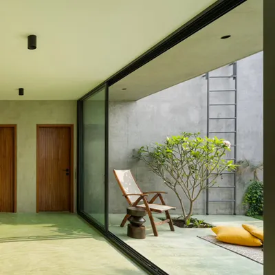 A large, floor-to-ceiling sliding glass door opens onto a serene private courtyard. The seamless transition from the green oxide floor inside to the outdoor patio extends the living space and invites nature indoors.