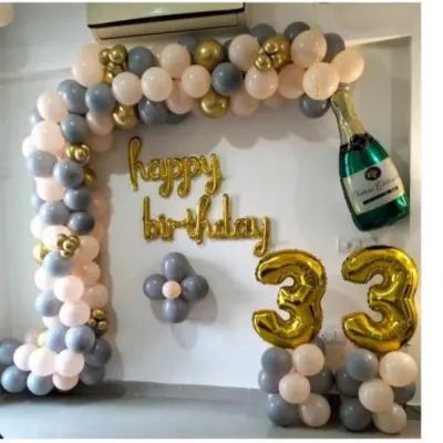 A classy 33rd birthday decoration with a balloon arch in grey, peach, and gold. The setup includes "Happy Birthday" foil letters and a champagne bottle balloon.