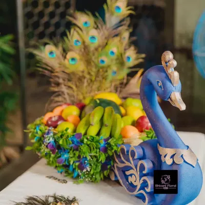 A custom peacock basket, or 'tokri', decorated with fresh flowers and filled with fruits for a baby shower ceremony. The peacock feathers add a touch of royalty.