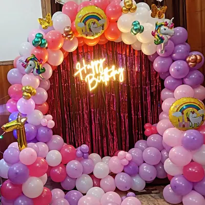 A magical Unicorn theme for a first birthday, featuring a circular balloon arch in pastel pinks and purples. The setup is completed with a "Happy Birthday" neon sign and unicorn-themed foil balloons.
