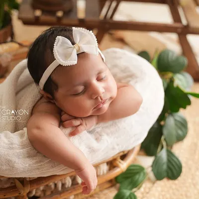 A newborn rests peacefully in a rustic wicker basket, adorned with a simple white bow. This style highlights the baby's natural beauty with earthy textures and soft lighting.