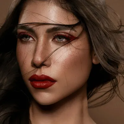 A portrait that is sharp, unapologetic, and real. The wind-swept hair adds a sense of movement and raw energy, contrasting with the precise, crimson makeup. This is editorial beauty that captures both strength and vulnerability.