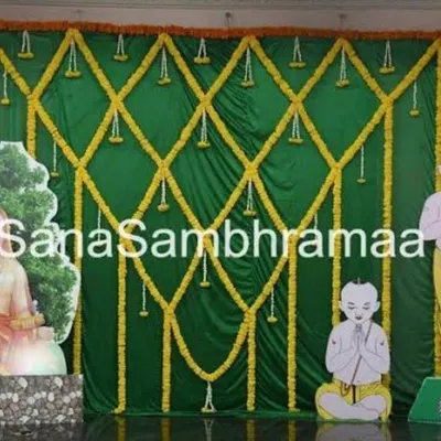 A traditional backdrop for a sacred thread ceremony (Upanayanam). The decor uses green drapes with marigold lattice work and features cutouts representing the religious theme.