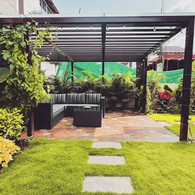 A modern metal pergola defines this comfortable outdoor lounge area. The slatted roof offers partial shade while maintaining an open, airy feel, creating a perfect spot for seating nestled within the garden.