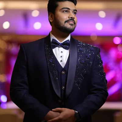 A client looking exceptionally dapper in his hand-crafted navy blue tuxedo. The intricate floral embroidery on the lapels and shoulders adds a unique, luxurious touch perfect for a reception or special event.