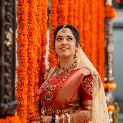 A breathtaking vision in red, this bride embodies traditional South Indian grace. Her look features classic temple jewellery and a radiant makeup look with defined eyes and a bold lip, perfectly complementing her vibrant Kanjivaram saree.