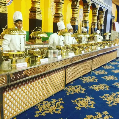 A view of our traditional 'Rajwadi' buffet line, featuring our uniformed staff ready to serve. The combination of ornate golden pillars in the venue and our polished brass dishes creates an unforgettable, regal dining atmosphere for your wedding.