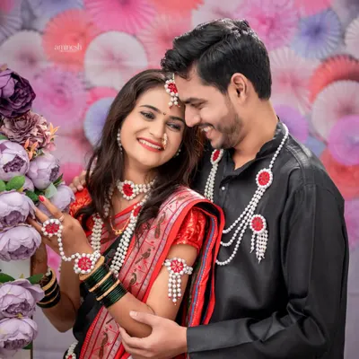 A couple dressed for Makarsankranti shares a candid, smiling moment against a backdrop of purple and pink flowers. These couple portraits capture the joy of the festival.