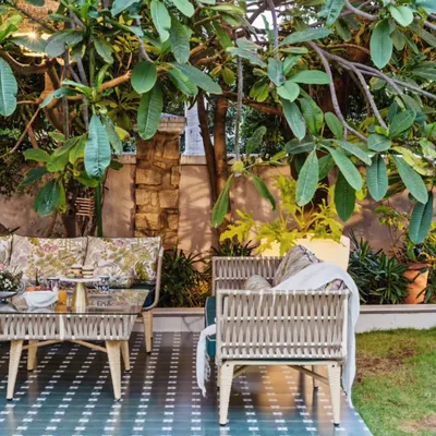 A perfect spot for morning coffee in a lush garden. The custom-made woven furniture and patterned tile deck are nestled under a canopy of green leaves, creating a serene and magical retreat.