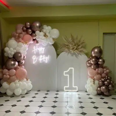 A stunningly modern first birthday setup in rose gold, blush, and white. The clean arched backdrops, neon sign, and organic balloon garlands create a sophisticated and trendy look.