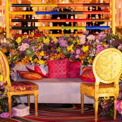 A burst of color for a Mehendi seating area, featuring a backdrop of multi-colored panels and a profusion of vibrant flowers, set against the royal architecture of Shiv Niwas Palace.