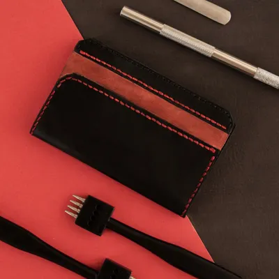 The essential tools for leatherworking laid out next to a finished cardholder. In our workshop, you'll learn to use these tools to cut, punch, and stitch leather into a professional-quality product.