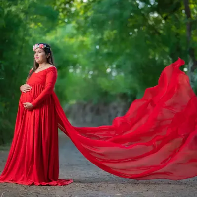 The drama of a long, flowing red gown looks incredible outdoors. The fabric catches the light and breeze, creating a stunning contrast against the natural green background of this rustic path.