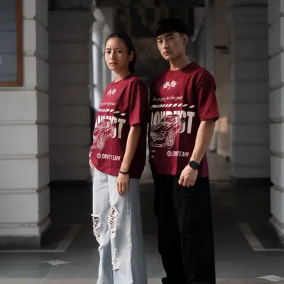A shot featuring both male and female models to showcase the unisex appeal of the graphic tee. The symmetrical pose in this architectural corridor creates a strong, balanced image for a brand campaign.