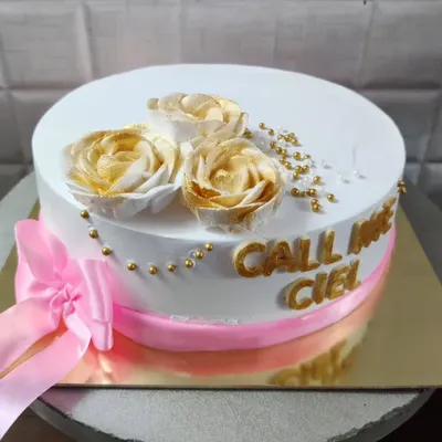 An elegant white cake with "Call me Ciel" written in gold. The design is finished with a pink ribbon and beautiful golden-dusted buttercream roses.