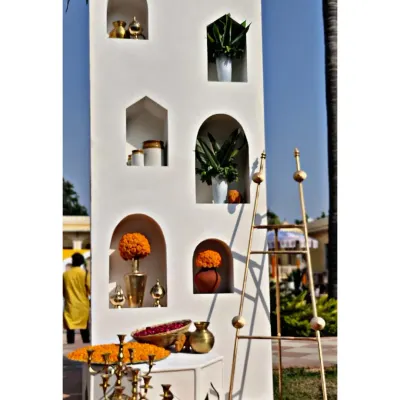 A detail of the Haldi ceremony entrance, showing the clean white structure with arched niches filled with marigold arrangements and brass pots. This is how we blend modern design with traditional elements.