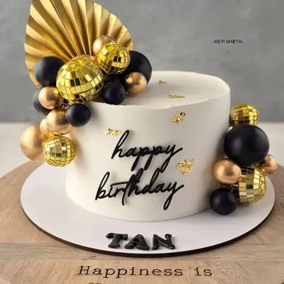 A chic black and gold birthday cake. The clean white whipped cream provides a perfect canvas for the mini disco balls and gold fan accent.