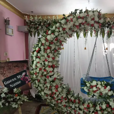 A full view of our highly requested naming ceremony decor. This design features a large crescent moon arch covered in white and red flowers, with a beautifully decorated cradle (thottilu) suspended in the center.