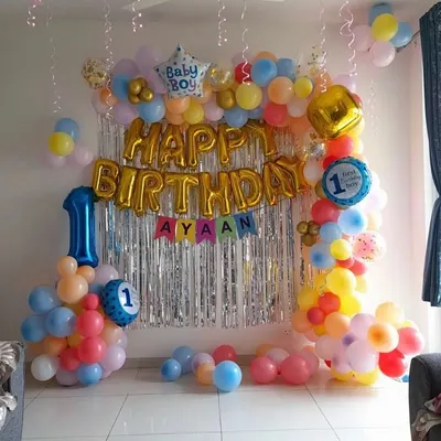 A classic birthday decoration perfect for a living room. This setup includes a 'Happy Birthday' foil balloon banner, a shimmer curtain, and a colorful balloon frame.