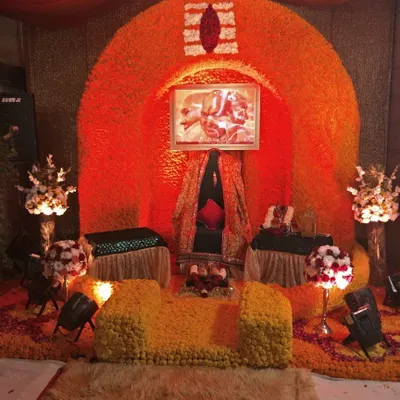 A vibrant Ganesh Chaturthi decoration. The gaddi is set inside a large arch made entirely of fresh orange and yellow marigolds, with a Tripundra symbol at the top, creating a bright and auspicious space for Ganpati Bappa.