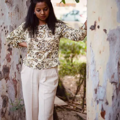 A full-length look at the Bagru print top paired with comfortable trousers. The natural setting and relaxed posture help customers envision themselves wearing this outfit for a casual day out. This is a key shot for a lifestyle clothing lookbook.