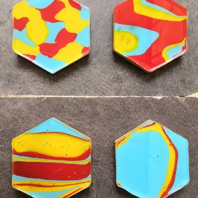 A set of four handmade coasters, each with a completely unique abstract design in primary colors. They are coated with resin for a glossy, durable finish. These are a fun way to add art to your home.