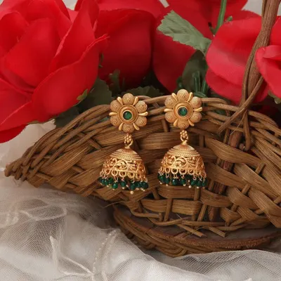 A lifestyle shot of traditional gold jhumkas with green beads, elegantly placed in a basket with red roses to create a rich, festive context for the jewellery.
