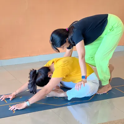 "Alone we can do so little, together we can do so much." A teacher assists a student in a forward bend, demonstrating the supportive nature of our community.