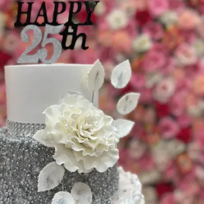 A close-up of the 25th-anniversary cake, focusing on the large, handcrafted white sugar flower and delicate silver leaves.