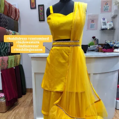A full view of the custom-designed yellow Haldi dress on a mannequin. This Indo-Western set includes a tiered skirt, crop top, and a delicate net dupatta with a ruffled border, perfect for pre-wedding festivities.