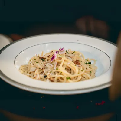 A beautifully plated dish of truffle spaghetti, finished with a delicate edible flower. This is an example of how we elevate a classic dish through thoughtful presentation and premium ingredients for a bespoke engagement menu.