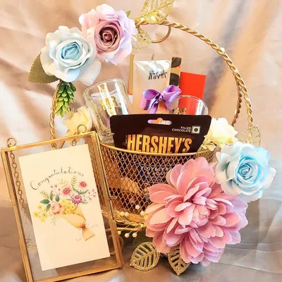 A sweet 'Congratulations' hamper to celebrate a special achievement. This golden basket is filled with chocolates, a personalized card in a glass frame, and beautiful pastel flowers.