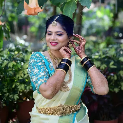 A beautiful moment of a bride getting ready for her big day. The makeup features a classic red lip and defined eyes, perfectly matching her cream and blue Kanjivaram saree and antique gold jewellery.
