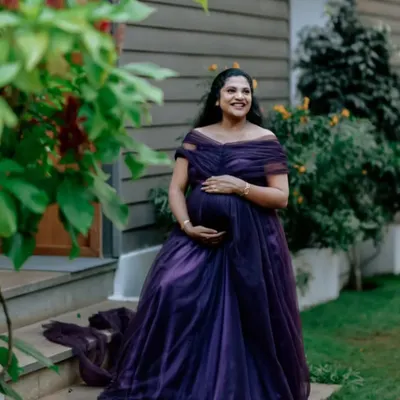 A happy client enjoying a quiet moment during her maternity shoot. The off-shoulder design and rich purple fabric of this rental gown are chosen for comfort and style.