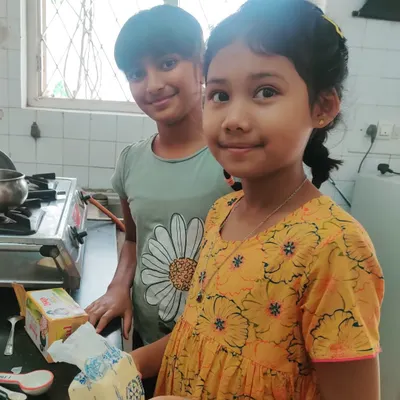 Two girls beam with pride after baking a two-layered vanilla piñata cake for the entire school. They managed the entire process themselves, from planning and shopping to mixing and decorating, experiencing the joy of self-directed work.