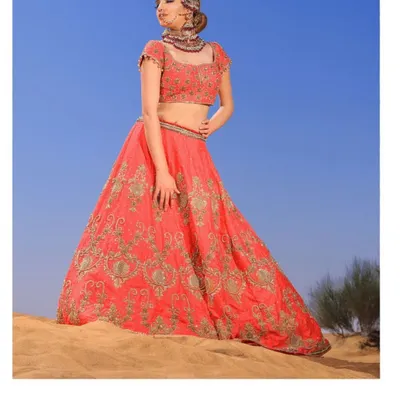 A magnificent coral-red bridal lehenga, heavily embellished with intricate zardosi work. This is a statement piece for the bride who desires a grand and opulent look for her wedding day.