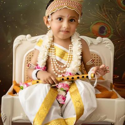 A stunning close-up of a young boy dressed as Lord Krishna, holding a flute. The detailed crown, pearl necklaces, and serene expression make this a powerful portrait.