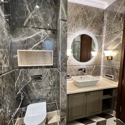 This powder room is a statement in luxury, featuring floor-to-ceiling grey Italian marble, a designer vanity with a vessel sink, and a beautiful backlit mirror.