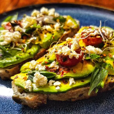 A delicious and healthy breakfast of homegrown avocado toast. It is topped with feta cheese, cherry tomatoes from the garden, and a sprinkle of chili flakes.