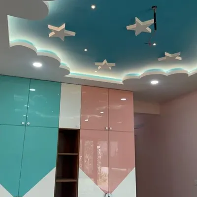A playful and practical kids' bedroom featuring a custom wardrobe in pastel pink and teal. The highlight is the cloud-and-star-themed false ceiling with integrated lighting, creating a magical sky effect.