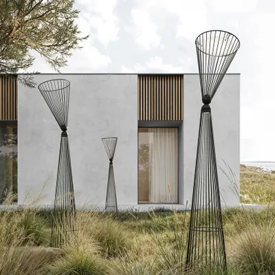 A grouping of Ikonika floor lamps by Karman in a landscaped garden. Their metal cage structure creates an airy visual volume that interacts beautifully with the surrounding grasses and modern architecture.