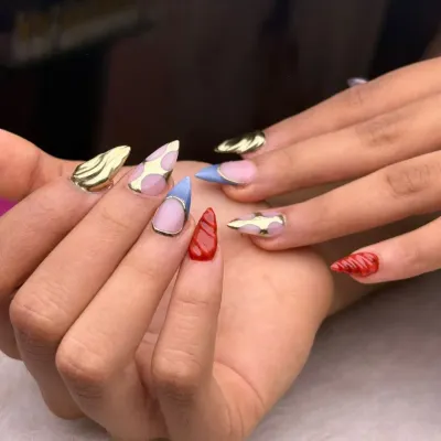 A playful and eclectic set that showcases a variety of techniques. It features gold chrome, cow print, textured red, and sheer blue nails for a fun, mismatched look that is full of personality.